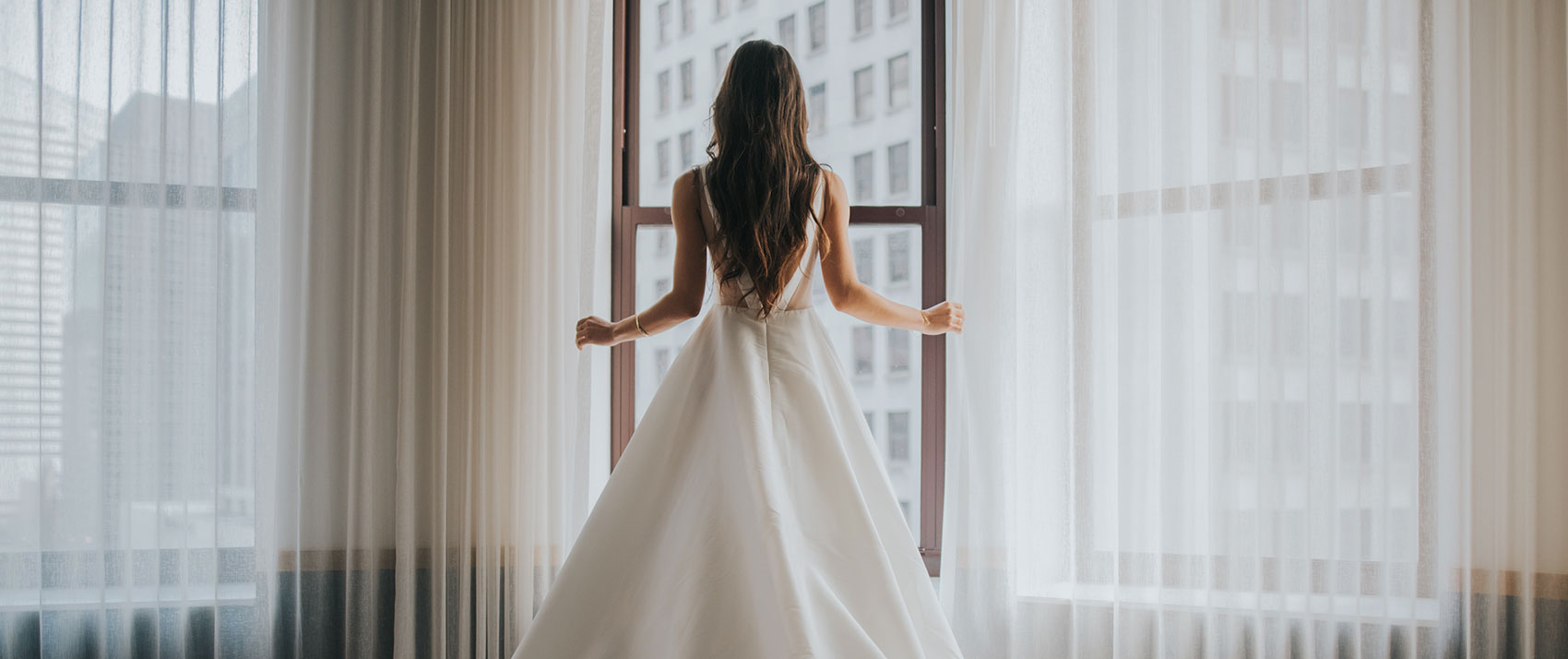 Vows There, Stay Here Brand Image. Bride standing in white wedding dress around window