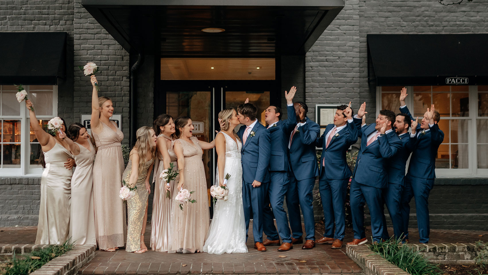 Couple kisses in front of Brice Hotel with wedding party